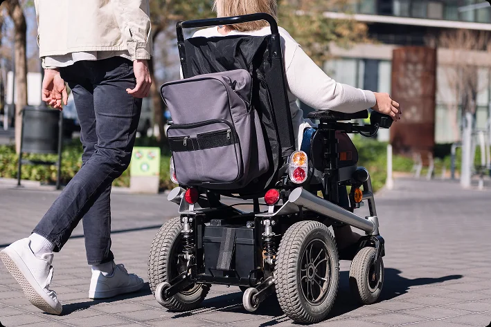 Person using a power wheelchair outdoors with a companion